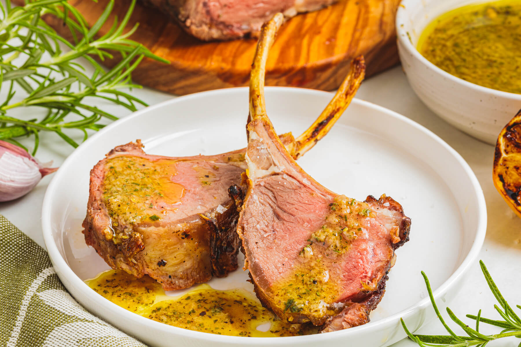 Two medium rare pink lamb chops drizzled with rosemary Dijon oil on a white plate.