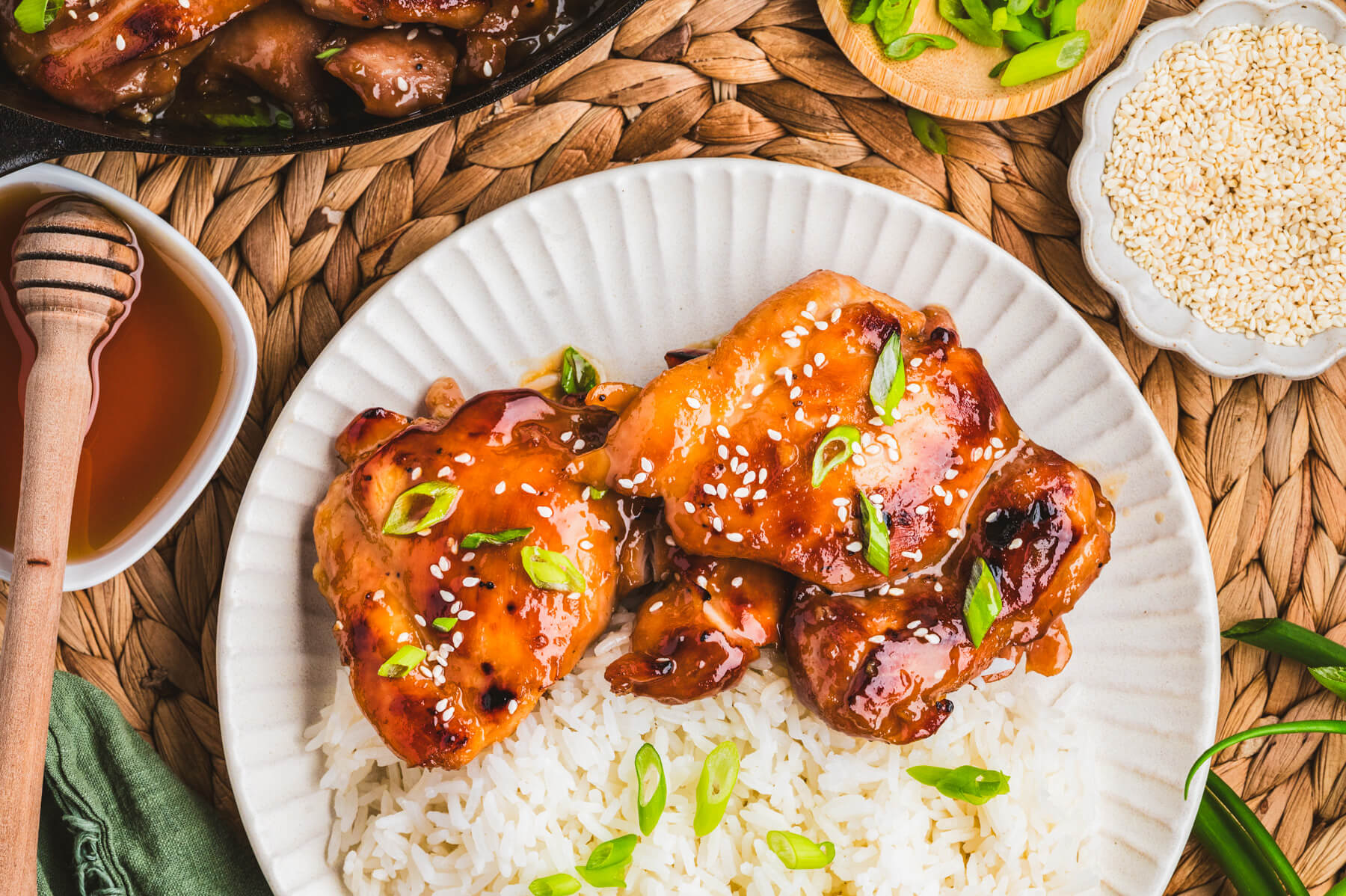 Two honey soy chicken thighs sit on top of a bed of rice garnished with sliced green onions and white sesame seeds.