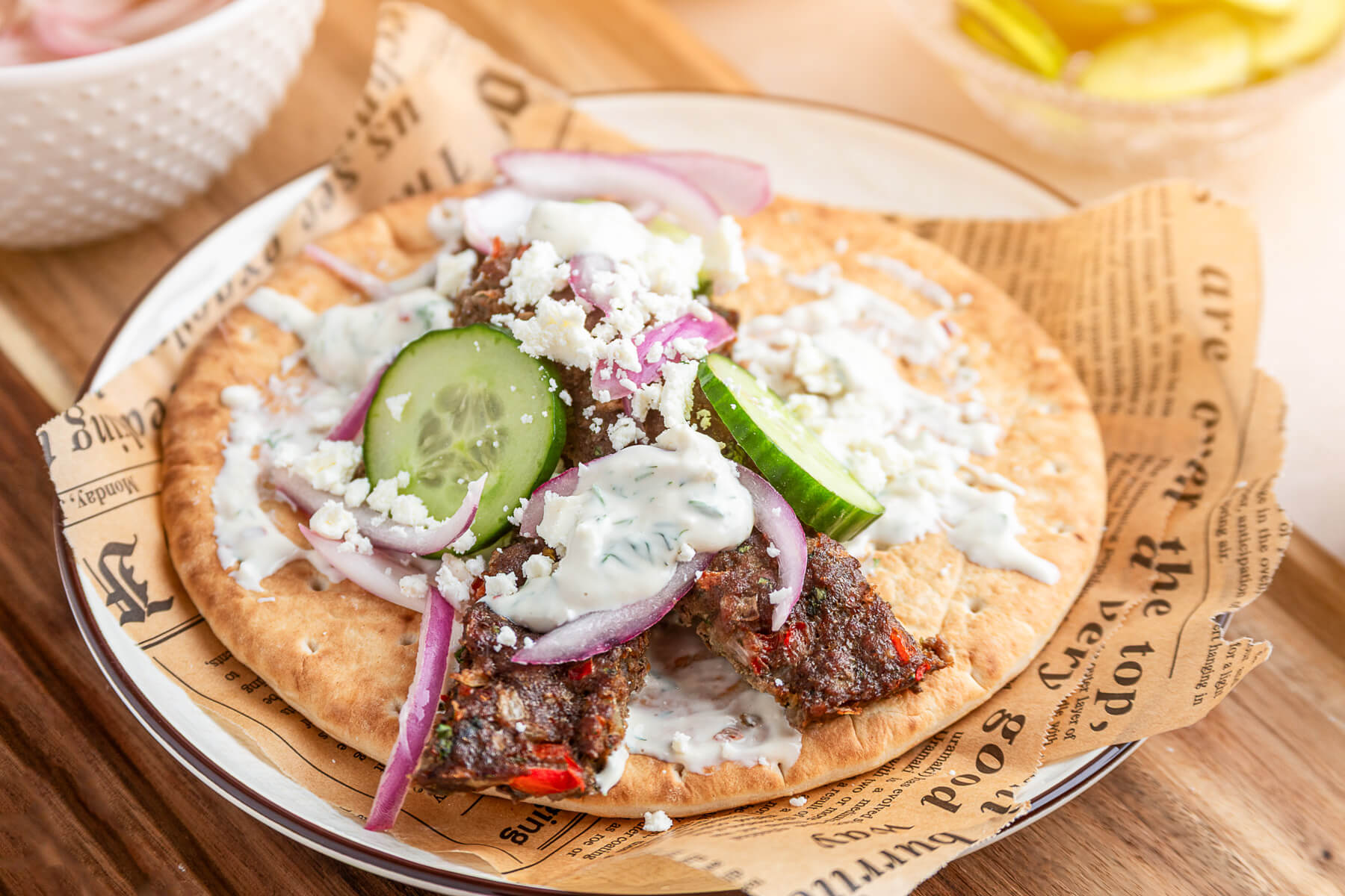 An open face pita topped with sheet pan kebabs, sliced cucumbers, red onions, feta cheese, and Greek yogurt tahini sauce.