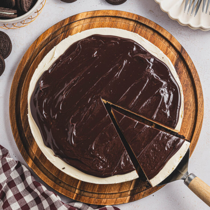 A whole Bailey's Cheesecake on a wooden serving board with a cake server holding a cut out slice.