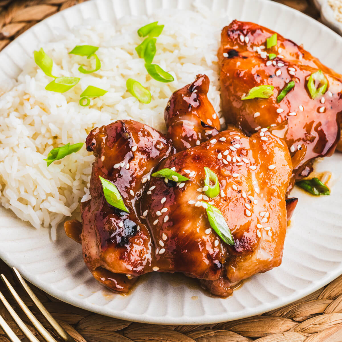 Two honey soy chicken thighs sit on top of a bed of rice garnished with sliced green onions and white sesame seeds.