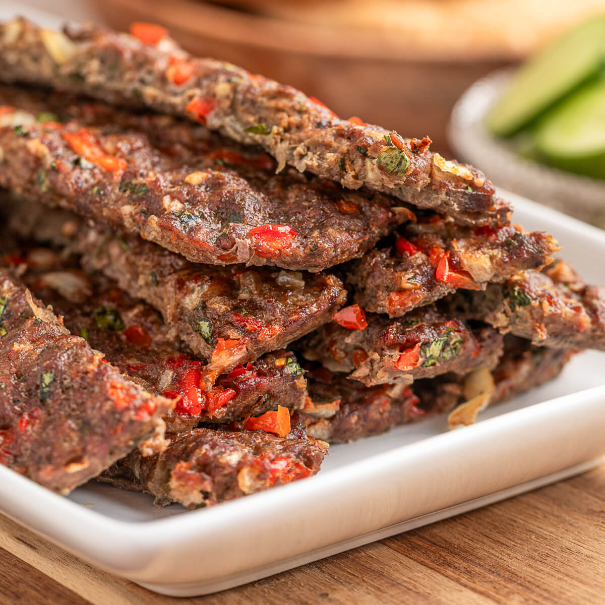 A pile of baked beef and lamb kebab studded with onions and red peppers on a large rectangular white plate.
