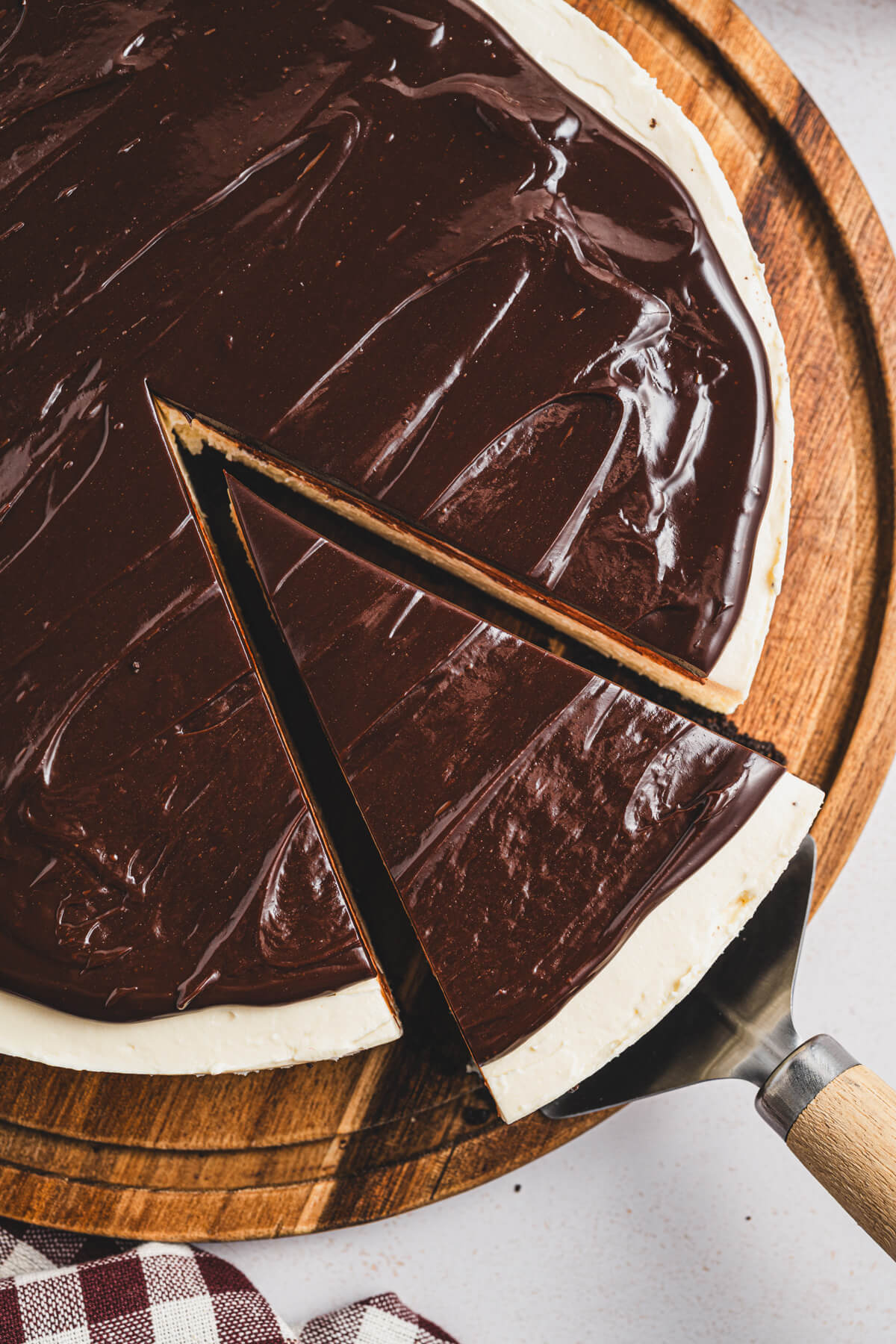 A whole Bailey's Cheesecake on a wooden serving board with a cake server holding a cut out slice.