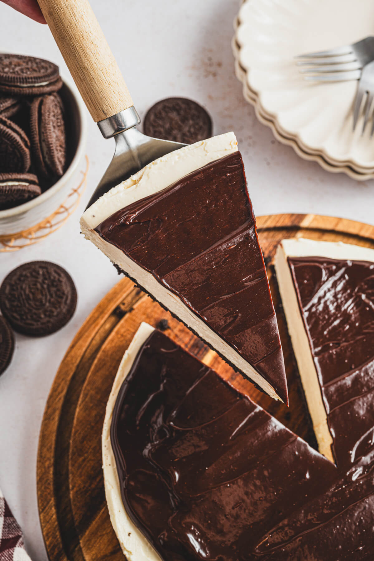 A whole Bailey's Cheesecake on a wooden serving board with a cake server holding a cut out slice.