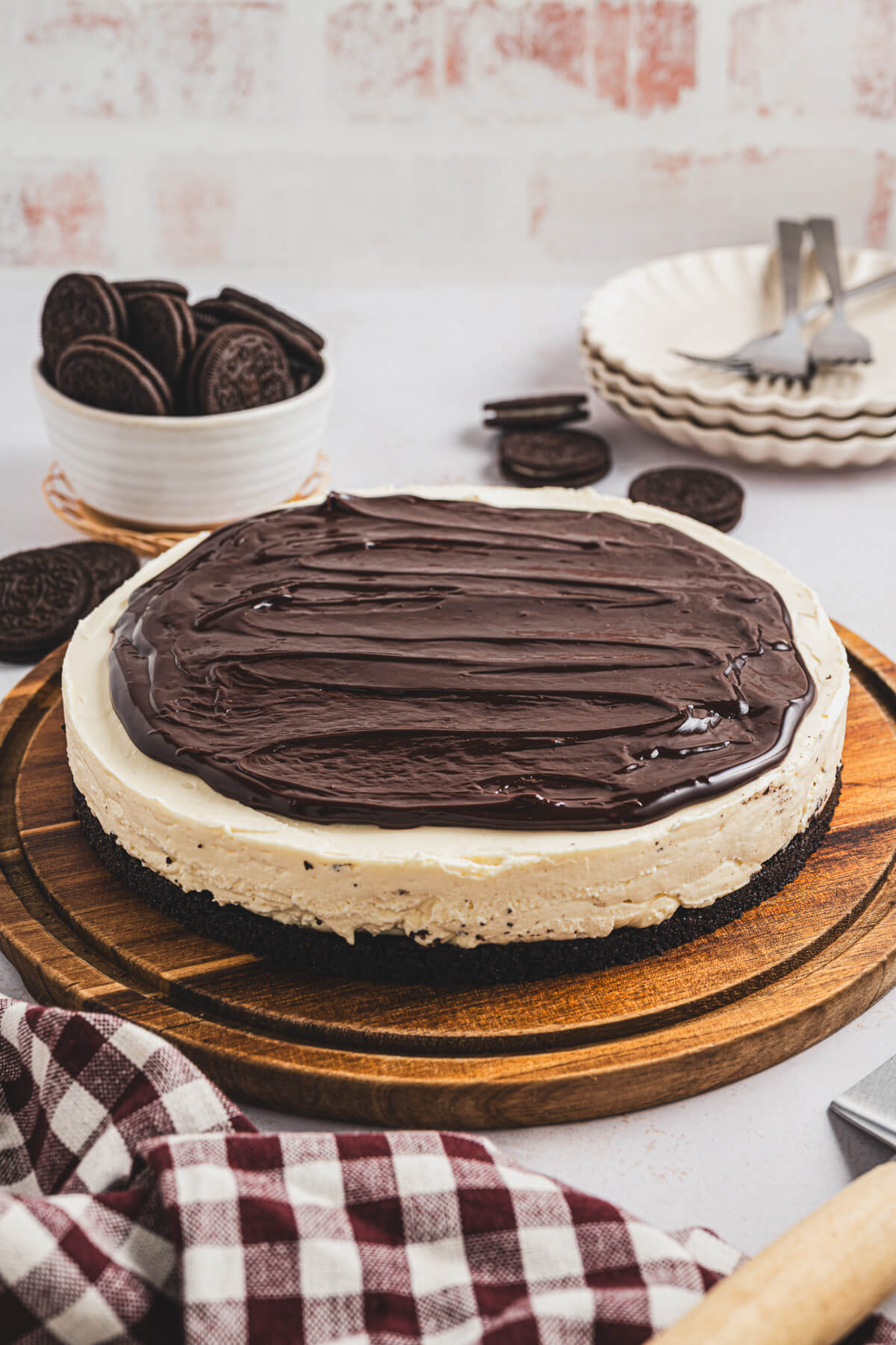 A whole no bake Bailey's Cheesecake topped with chocolate ganache on a wooden serving board.