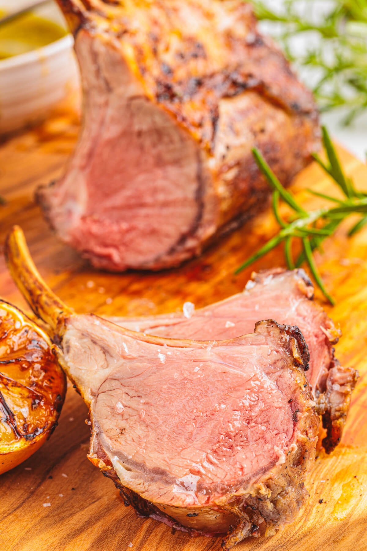 Two medium rare pink lamb chops freshly sliced from the whole rack on a wooden cutting board.