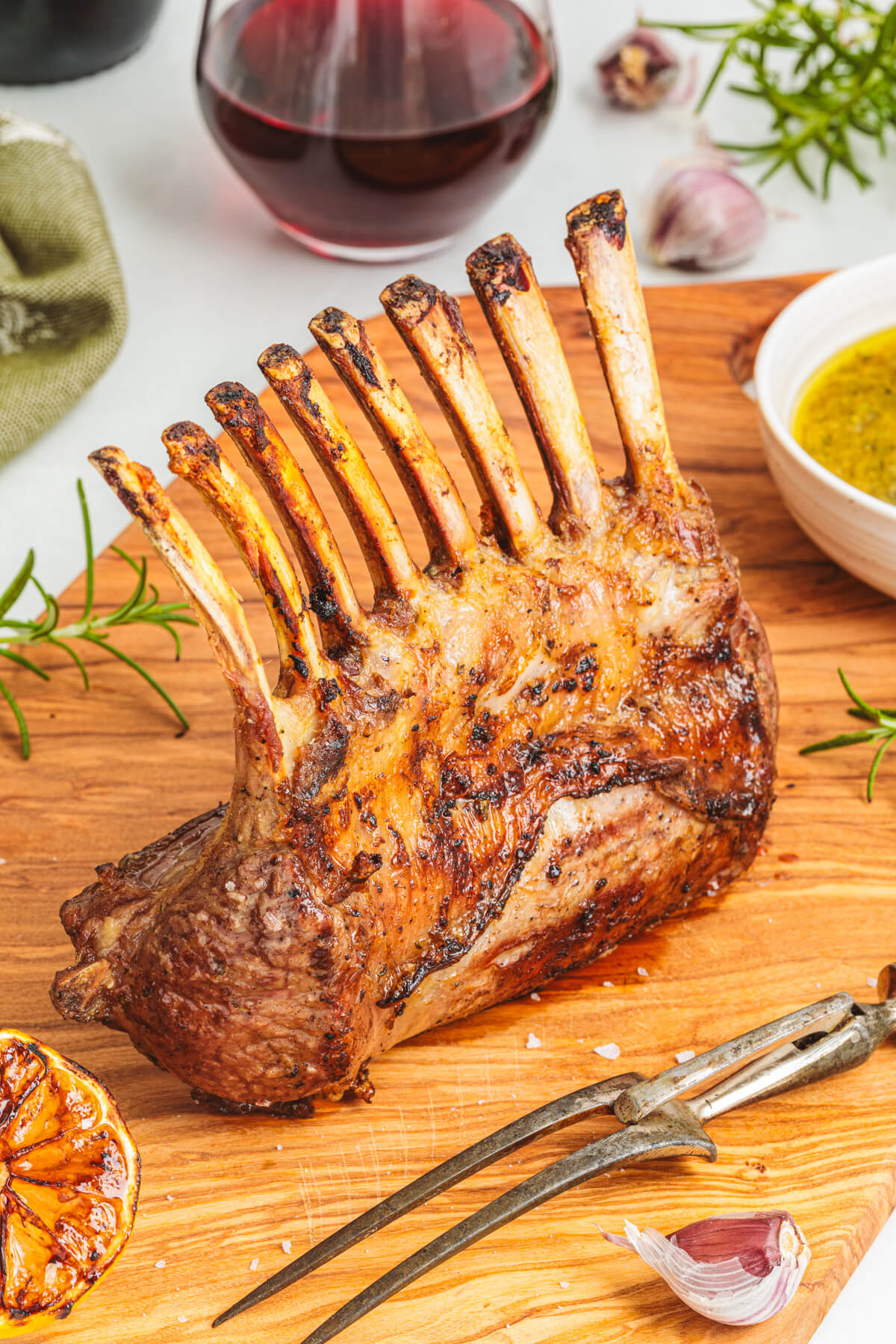 A perfectly grilled whole rack of lamb is ready to slice on a wooden cutting board. 