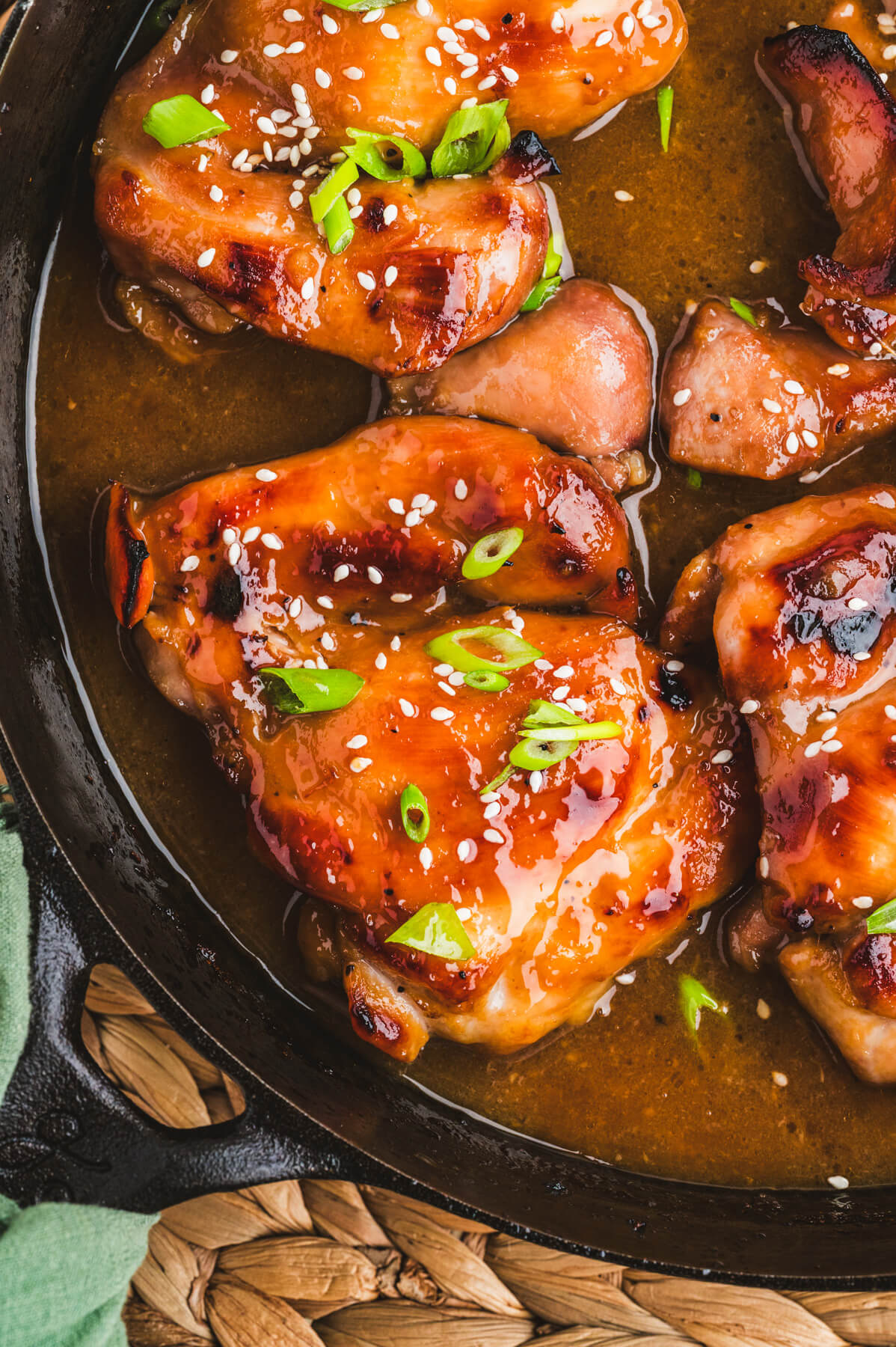 Glossy honey soy chicken thighs garnished with sliced green onions and white sesame seeds in a cast iron skillet.