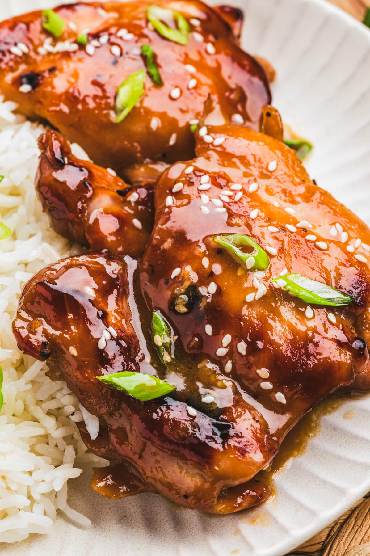 Two honey soy chicken thighs sit on top of a bed of rice garnished with sliced green onions and white sesame seeds.