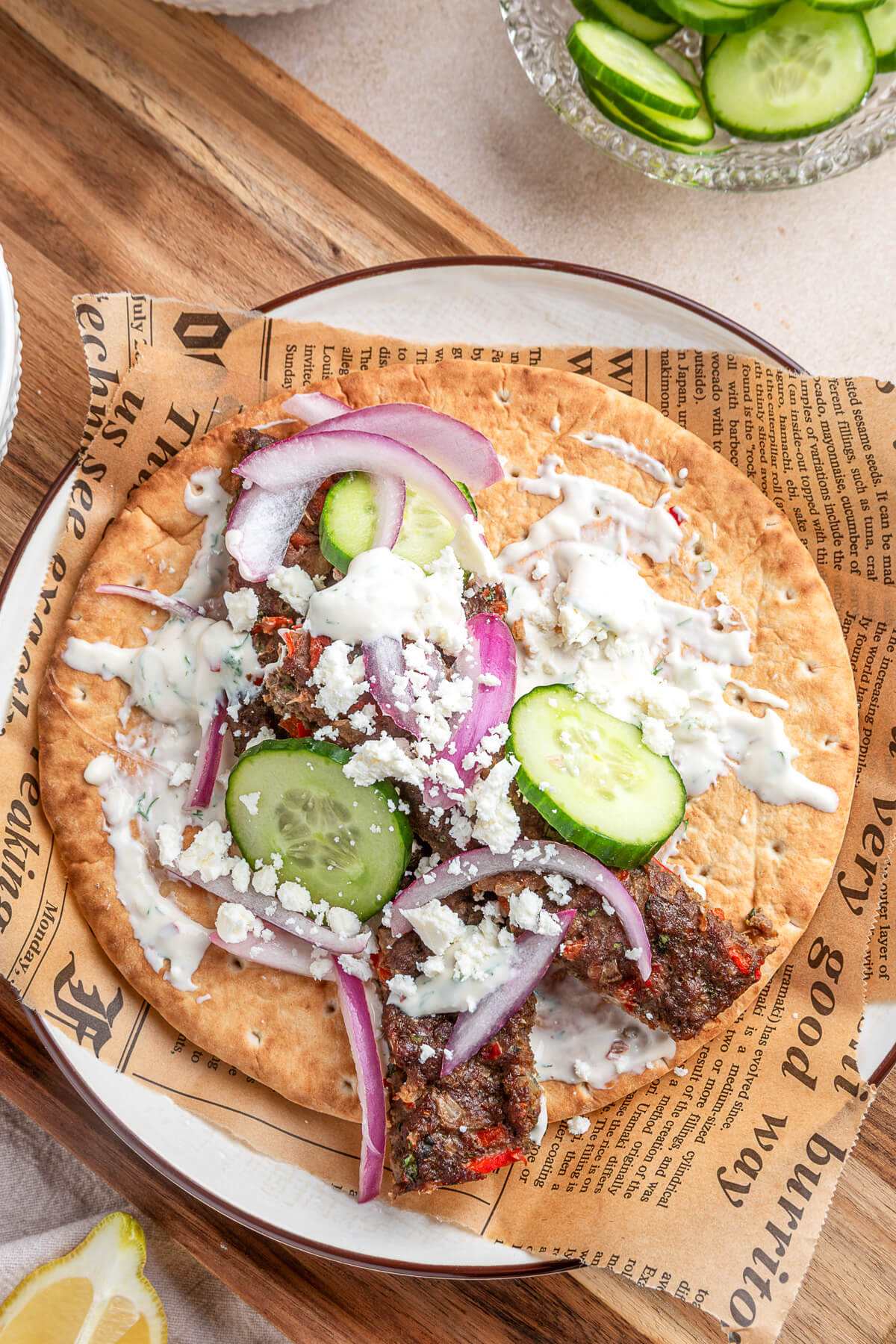 An open face pita topped with sheet pan kebabs, sliced cucumbers, red onions, feta cheese, and Greek yogurt tahini sauce.