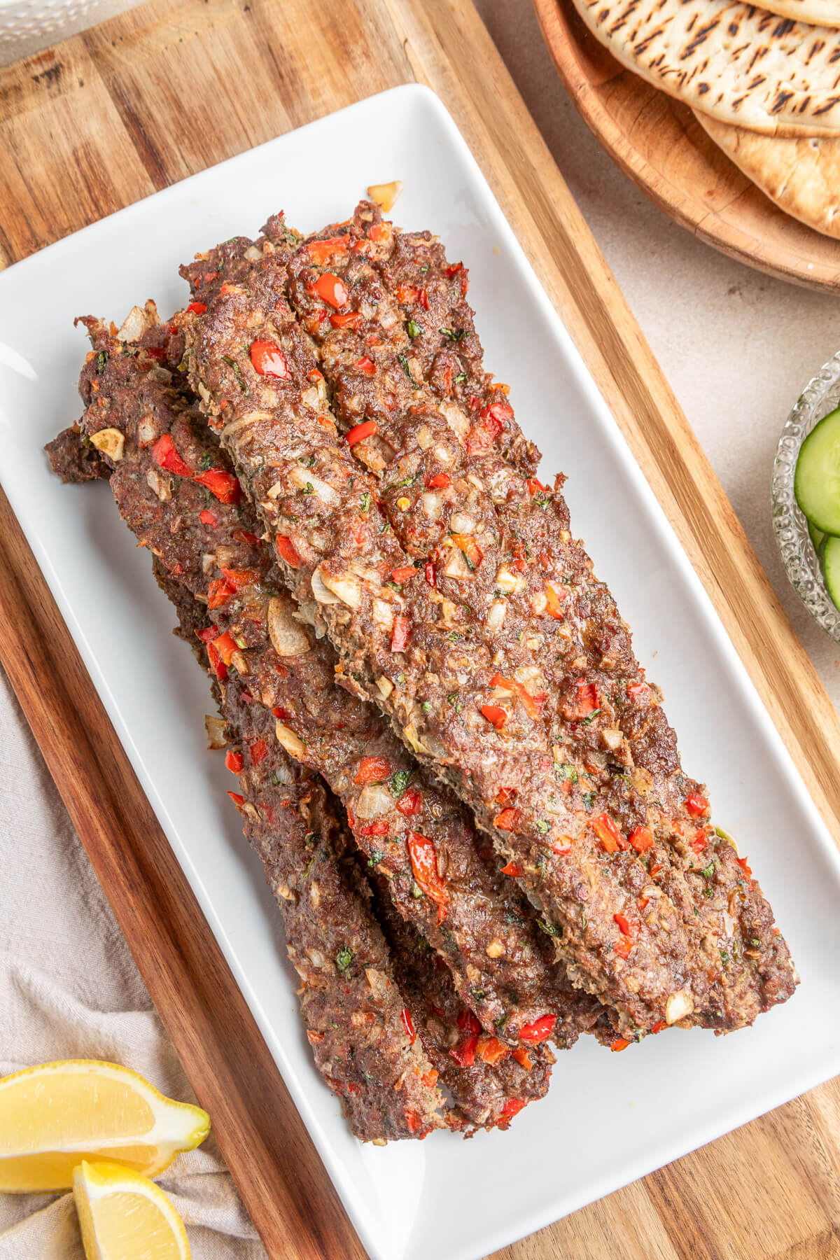 A pile of baked beef and lamb kebab studded with onions and red peppers on a large rectangular white plate. 