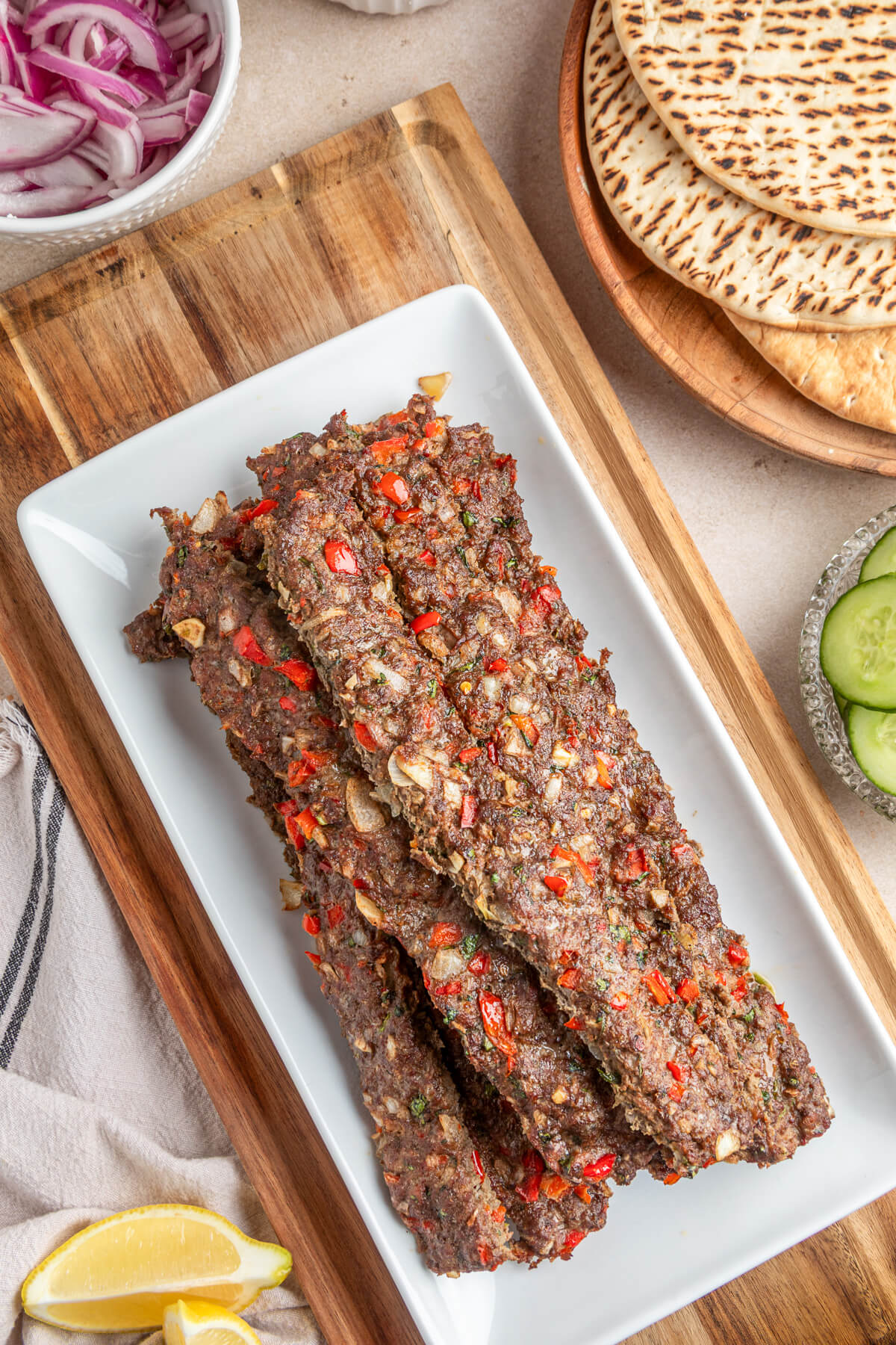 A pile of baked beef and lamb kebab studded with onions and red peppers on a large rectangular white plate.