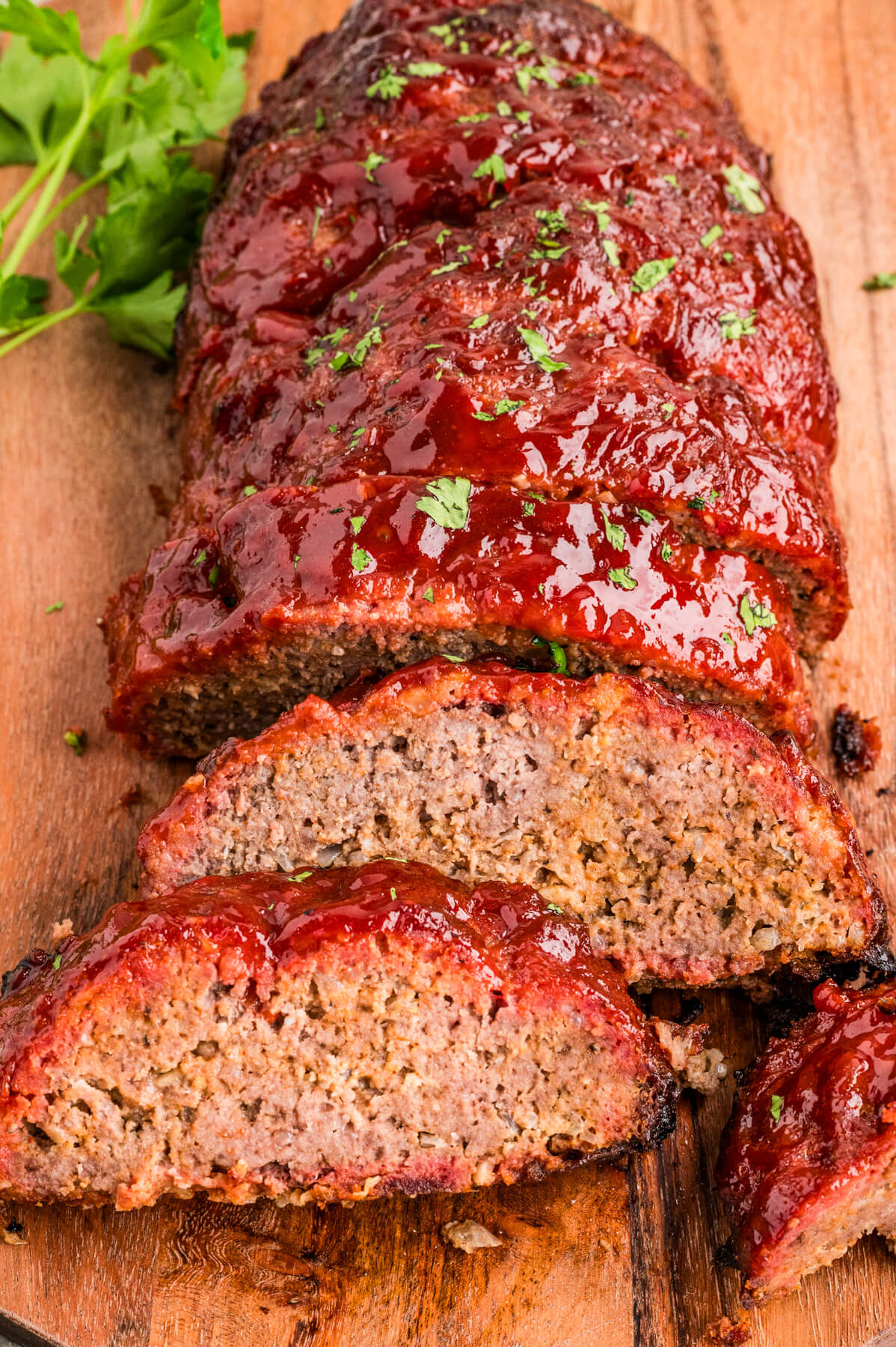 A half sliced shiny glazed smoked meatloaf on a wooden cutting board.
