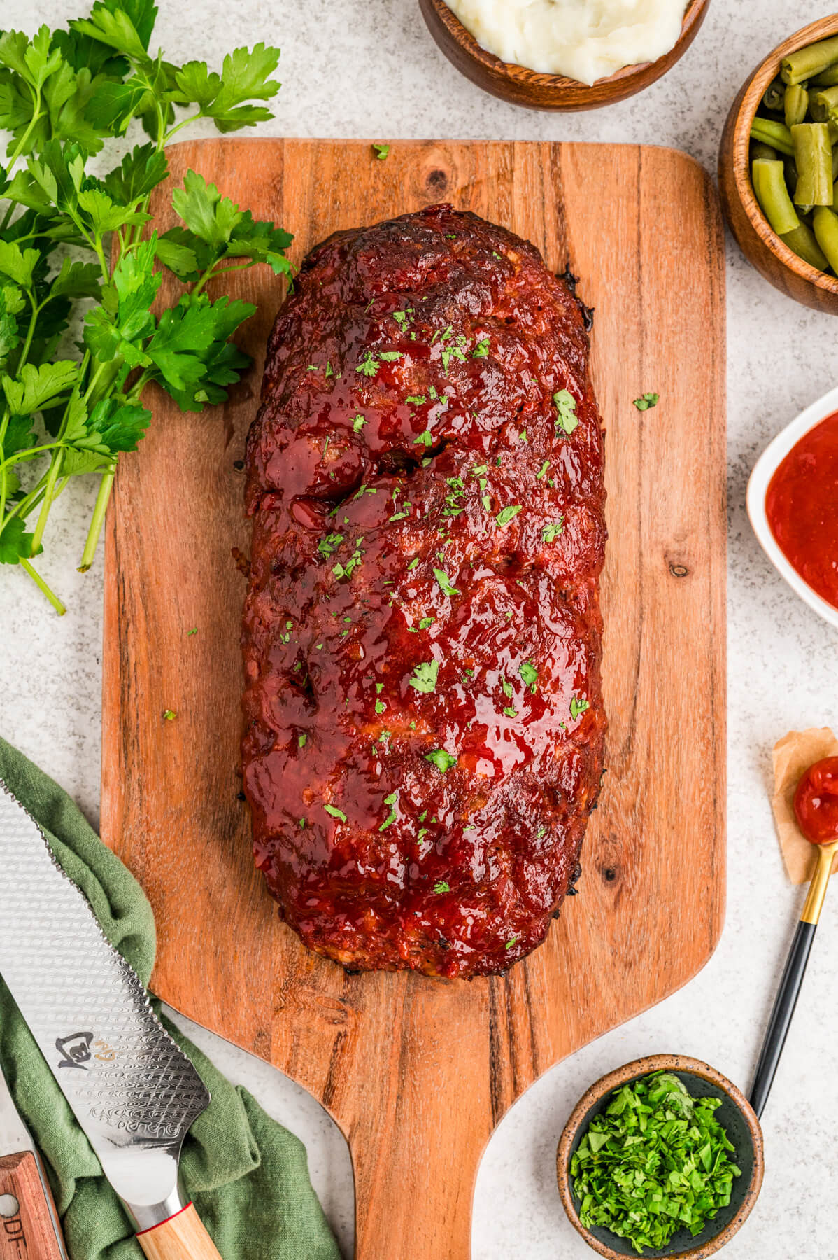 A whole shiny glazed smoked meatloaf on a wooden cutting board.