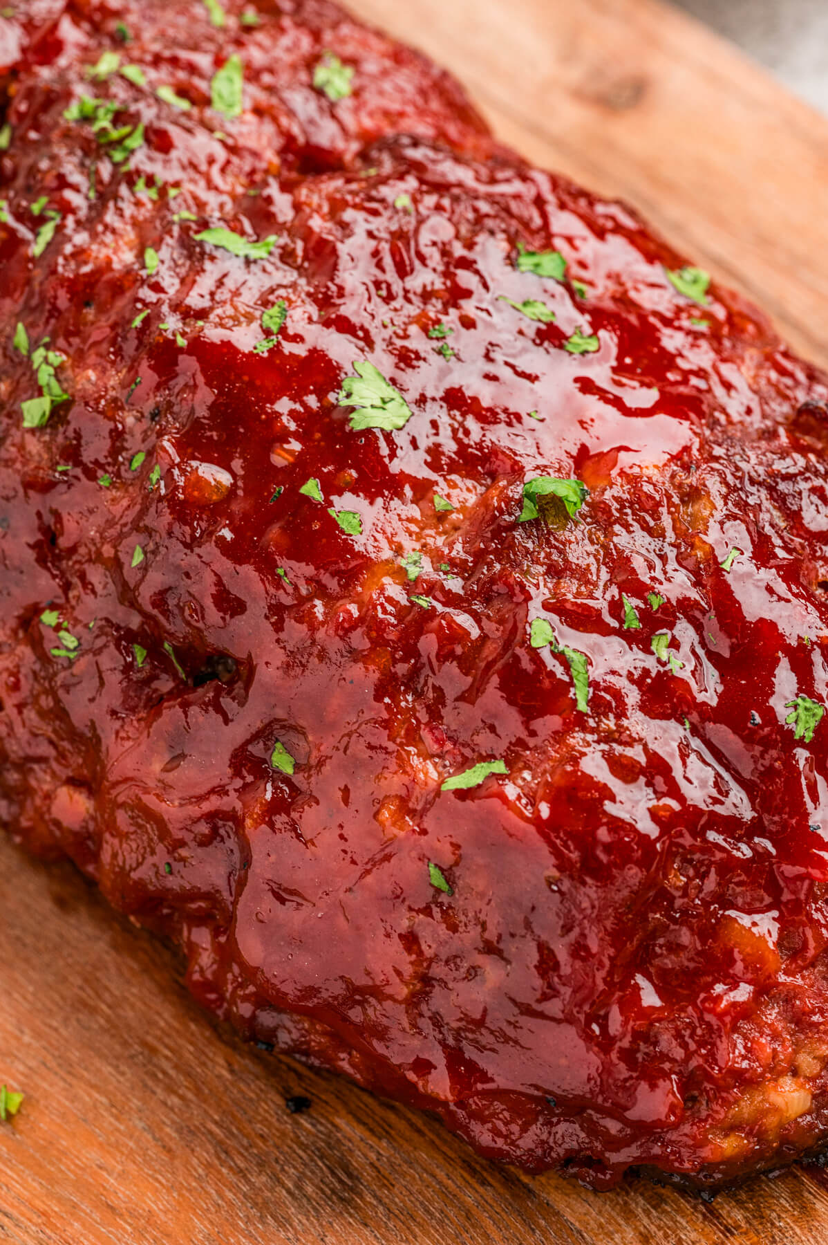 A whole shiny glazed smoked meatloaf on a wooden cutting board.