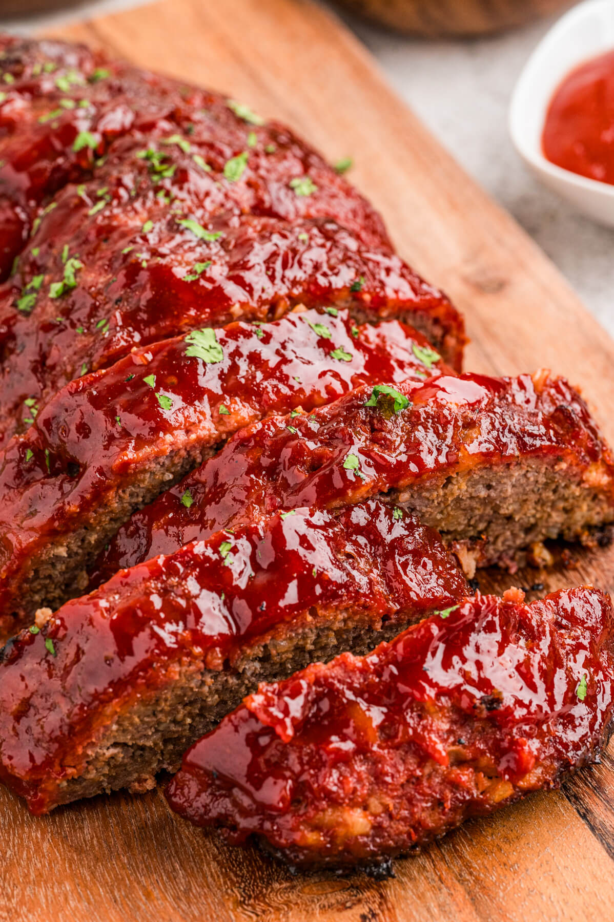 A half sliced shiny glazed smoked meatloaf on a wooden cutting board.