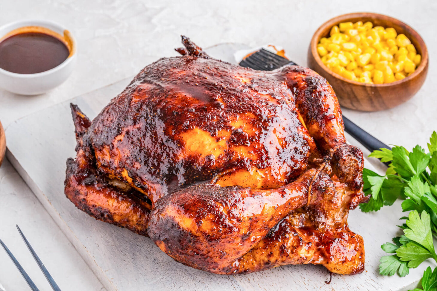 A whole Smoked BBQ Chicken glistening with glaze surrounded by dinner side dishes.