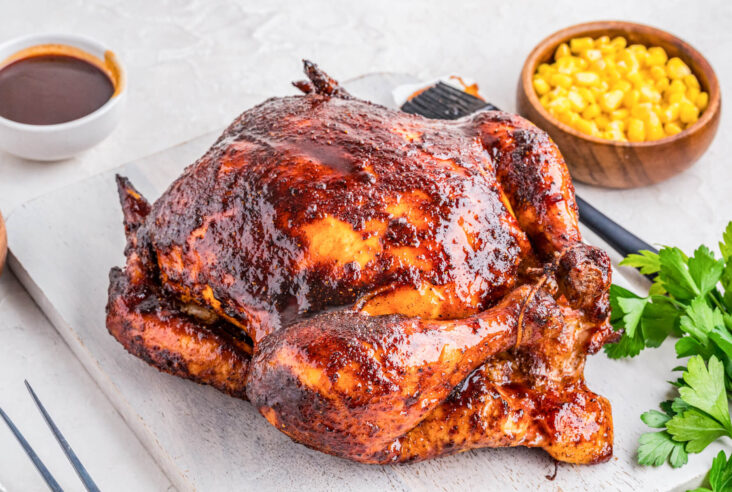 A whole Smoked BBQ Chicken glistening with glaze surrounded by dinner side dishes.