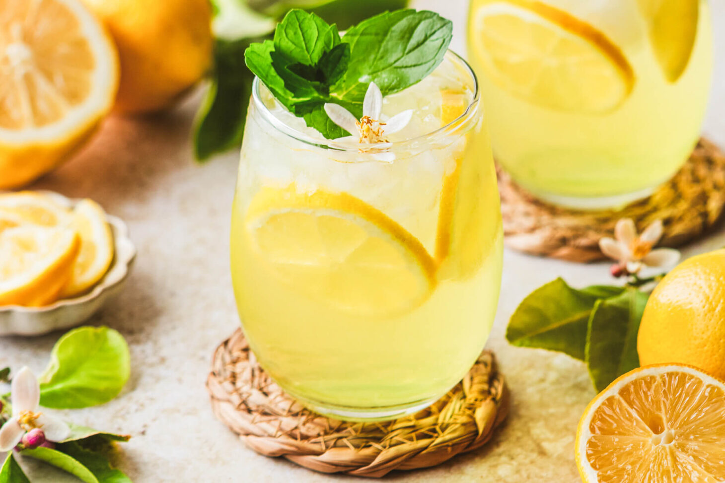 A sunny yellow cockail in a stemless wine glass garnished with fresh mint and lemon slices.