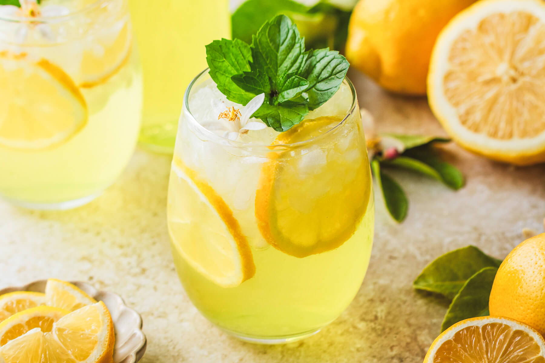 A sunny yellow cockail in a stemless wine glass garnished with fresh mint and lemon slices.