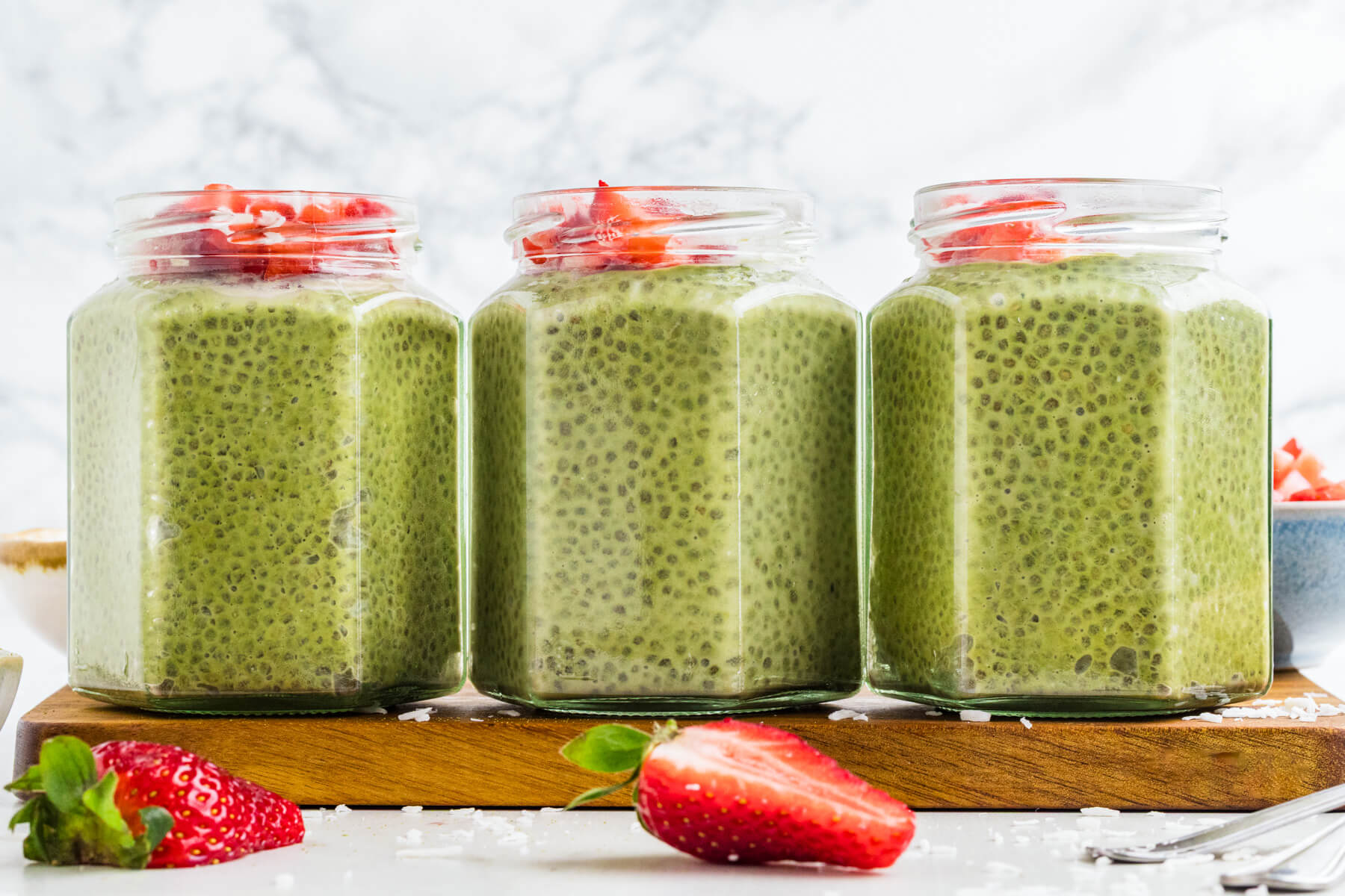 Three jars of vibrant green Match Chia Pudding topped with sliced strawberries and coconut flakes.