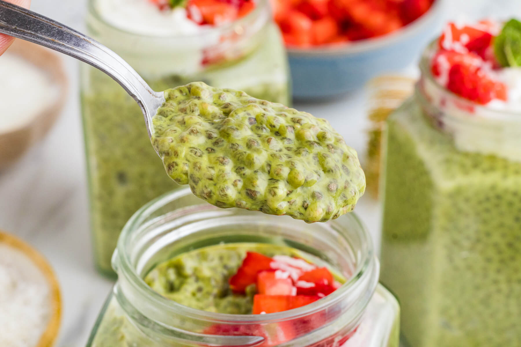 A spoon holding Matcha Chia Pudding showing the texture over a jar of pudding.
