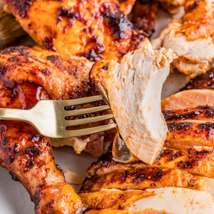 A juicy piece of smoked bbq chicken on a fork hovers above a serving platter of chicken.