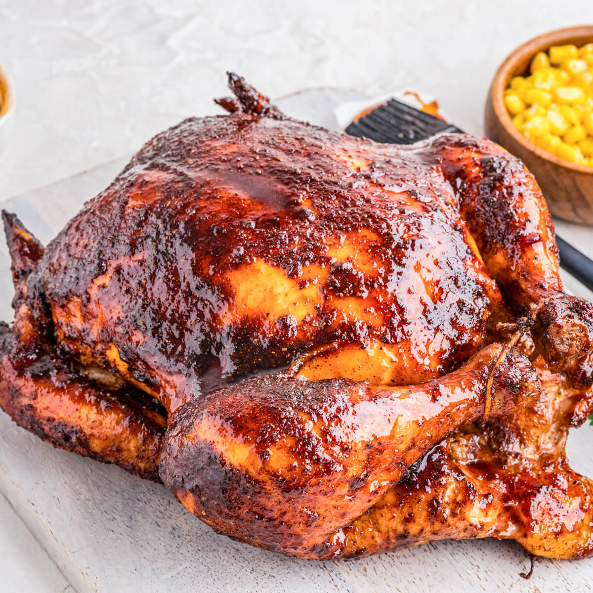 A whole Smoked BBQ Chicken glistening with glaze surrounded by dinner side dishes.