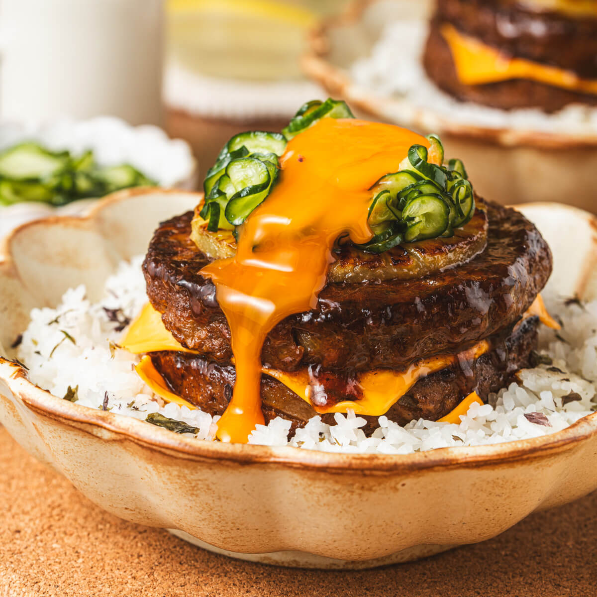 A two layer Japanese Hambagu steak dish piled high with American cheese, grilled pineapple, picked cucumber and topped with a flowing egg yolk on a bed of seasoned rice.