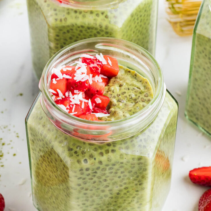 A jar of vibrant green Match Chia Pudding topped with sliced strawberries and coconut flakes.