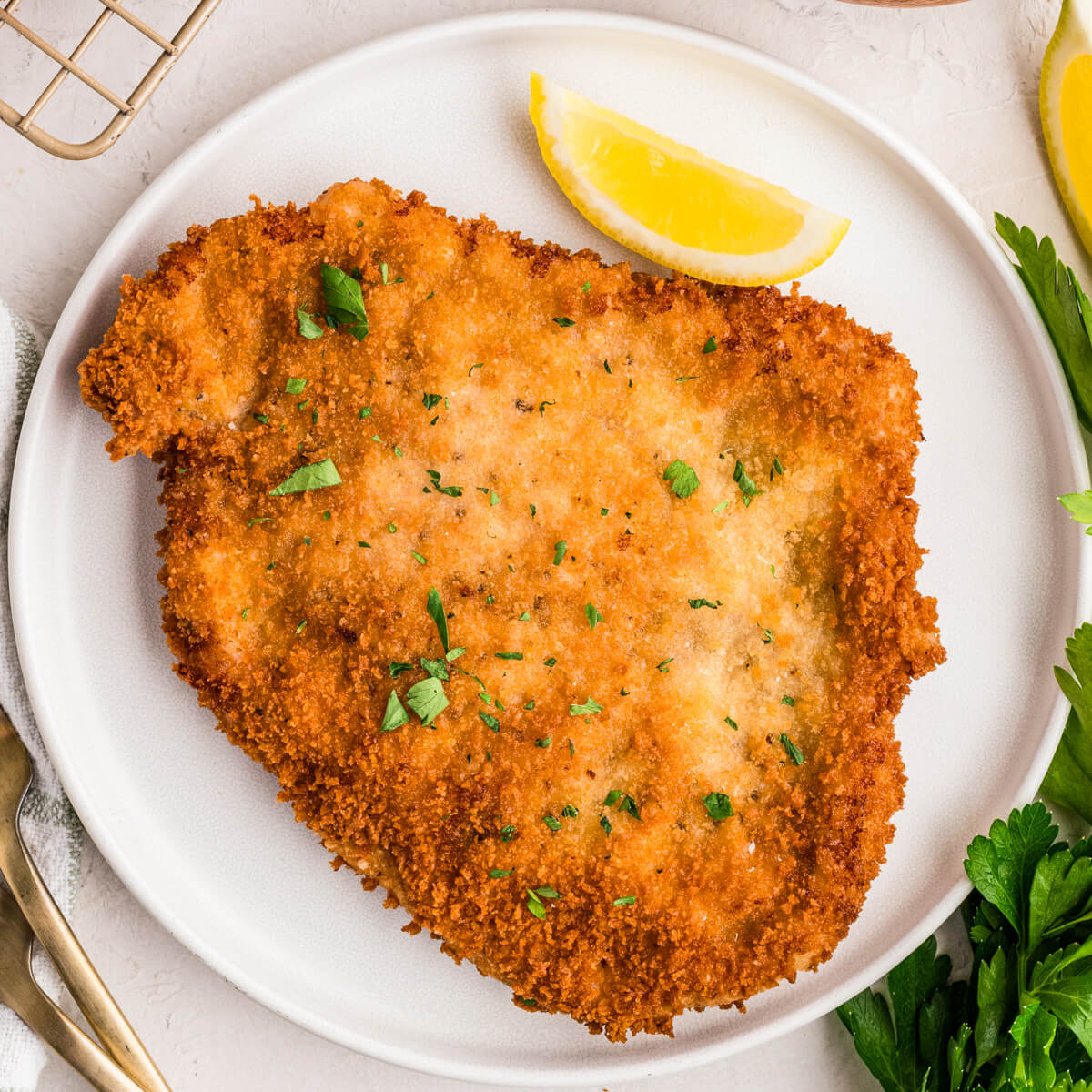 A golden brown fried pork schnitzel on a plate with a lemon wedge on a dinner table.