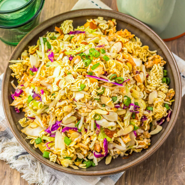 A brown bowl filled with ramen noodle salad featuring pulled rotisserie chicken, coleslaw mix, sesame seeds, and green onions.