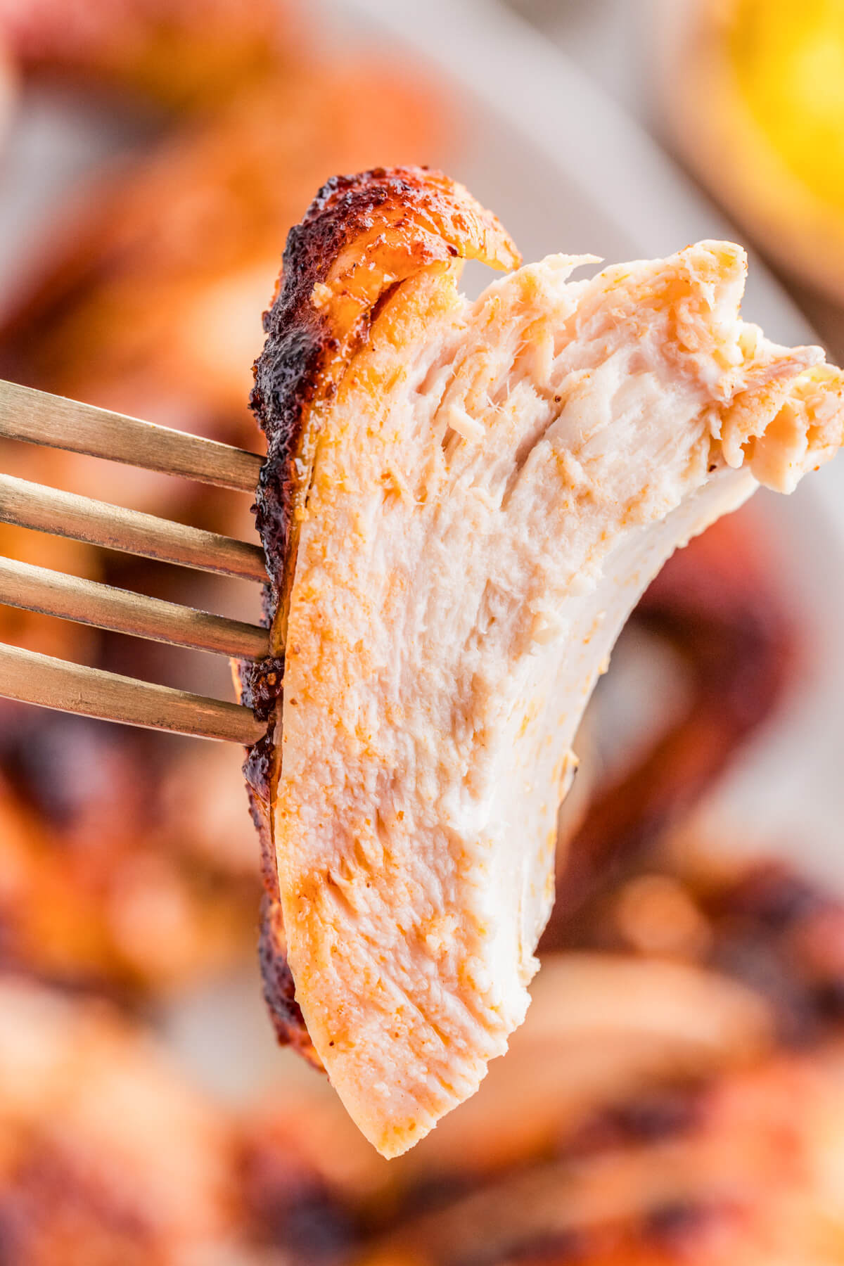 A juicy piece of smoked bbq chicken on a fork hovers above a serving platter of chicken.