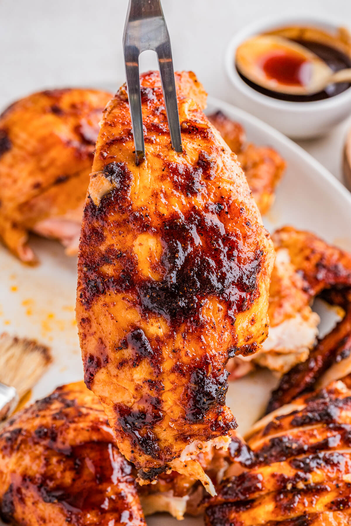 A juicy piece of smoked bbq chicken on a fork hovers above a serving platter of chicken.