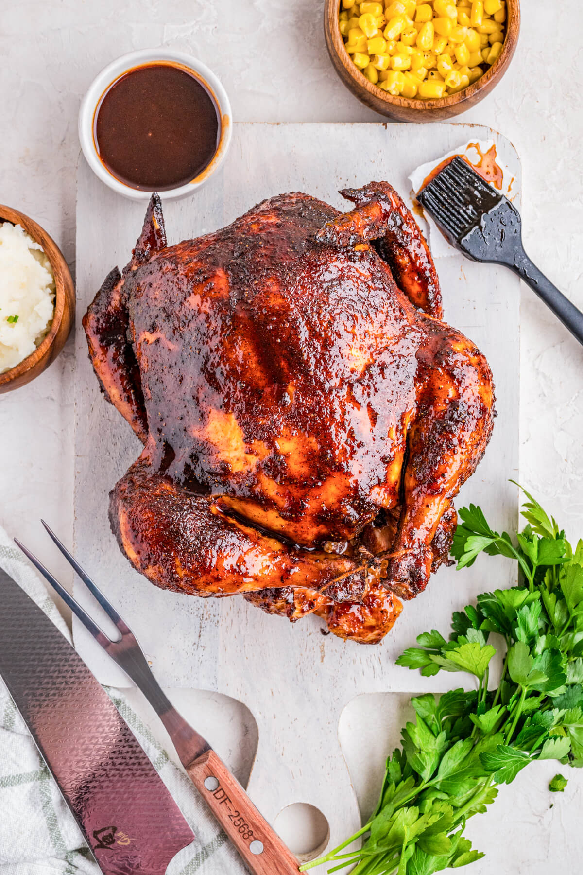 A whole Smoked BBQ Chicken glistening with glaze surrounded by dinner side dishes.