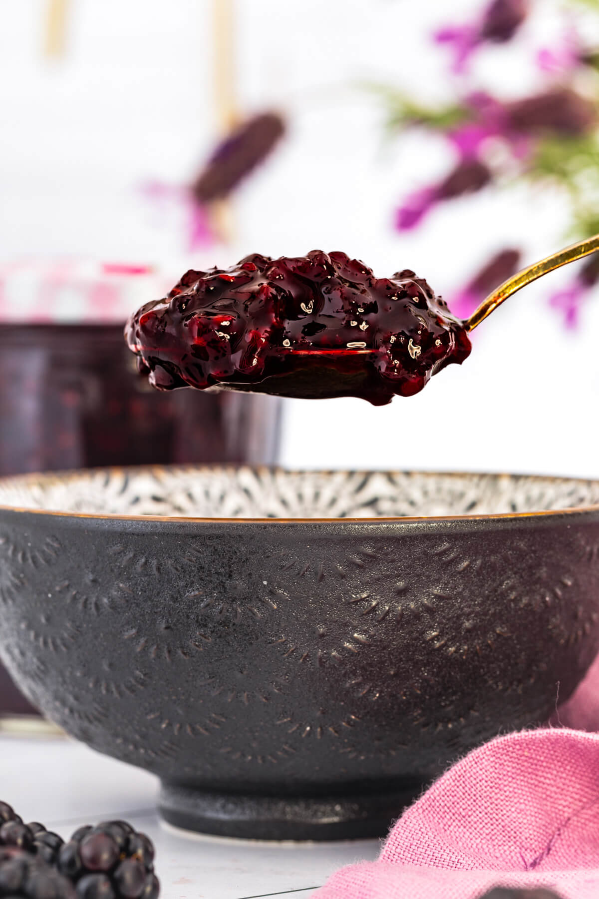 A spoon full of blackberry jam hovers over a bowl of the same jam.