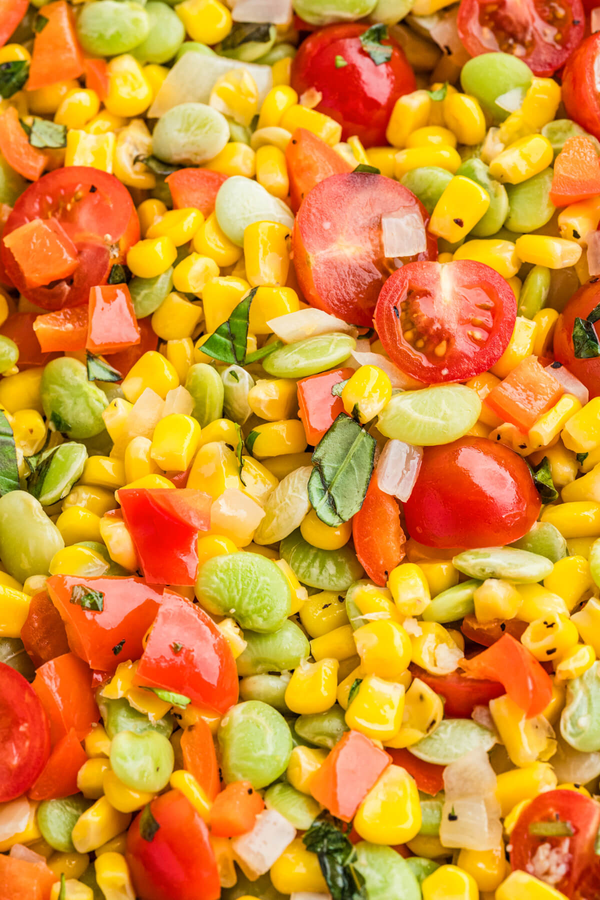 Vibrant yellow corn succotash featuring green lima beans, red bell peppers, cherry tomatoes, and fresh basil.