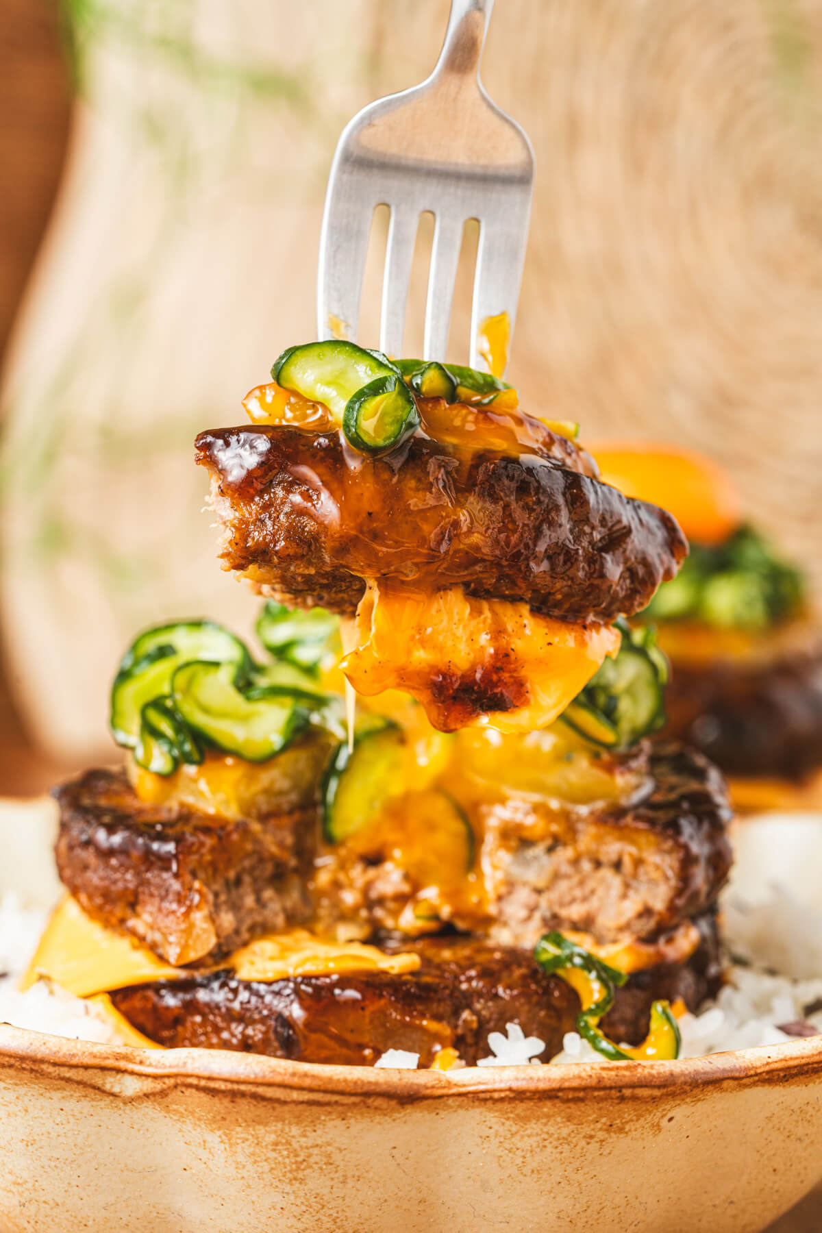 A fork lifts a bite of Japanese hambagu steak, grilled pineapple, pickled cucumber, and American cheese dripping with teriyaki sauce.