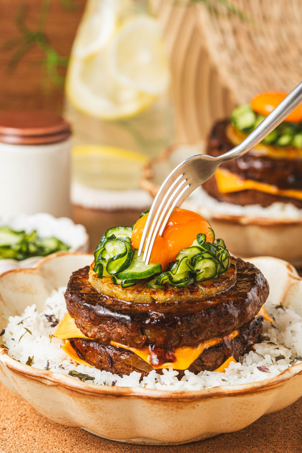 A fork is about to break the raw egg yolk which tops a multilayered Japanese Hambagu steak. 