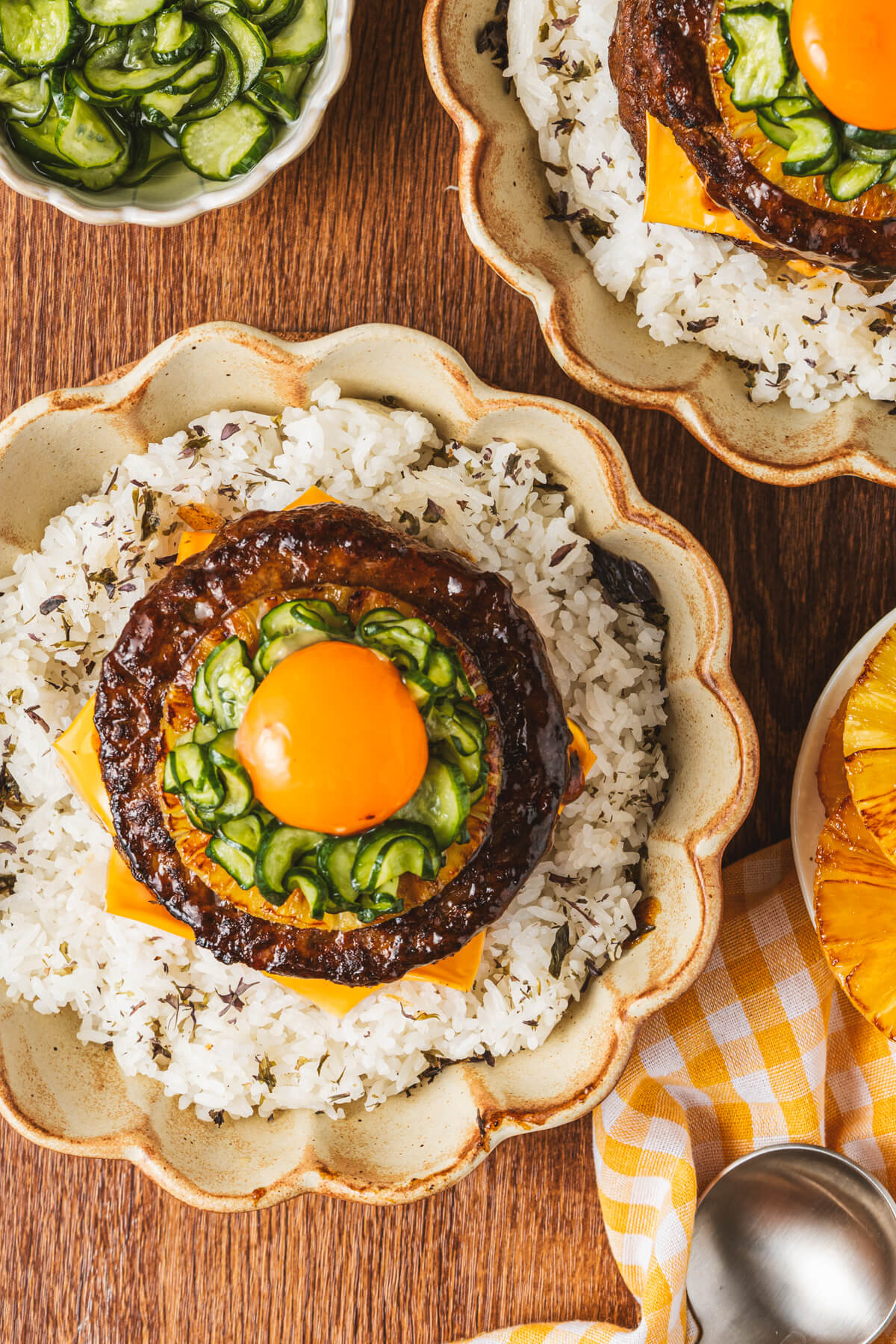 A two layer Japanese Hambagu steak dish piled high with American cheese, grilled pineapple, picked cucumber and topped with an egg yolk on a bed of seasoned rice.