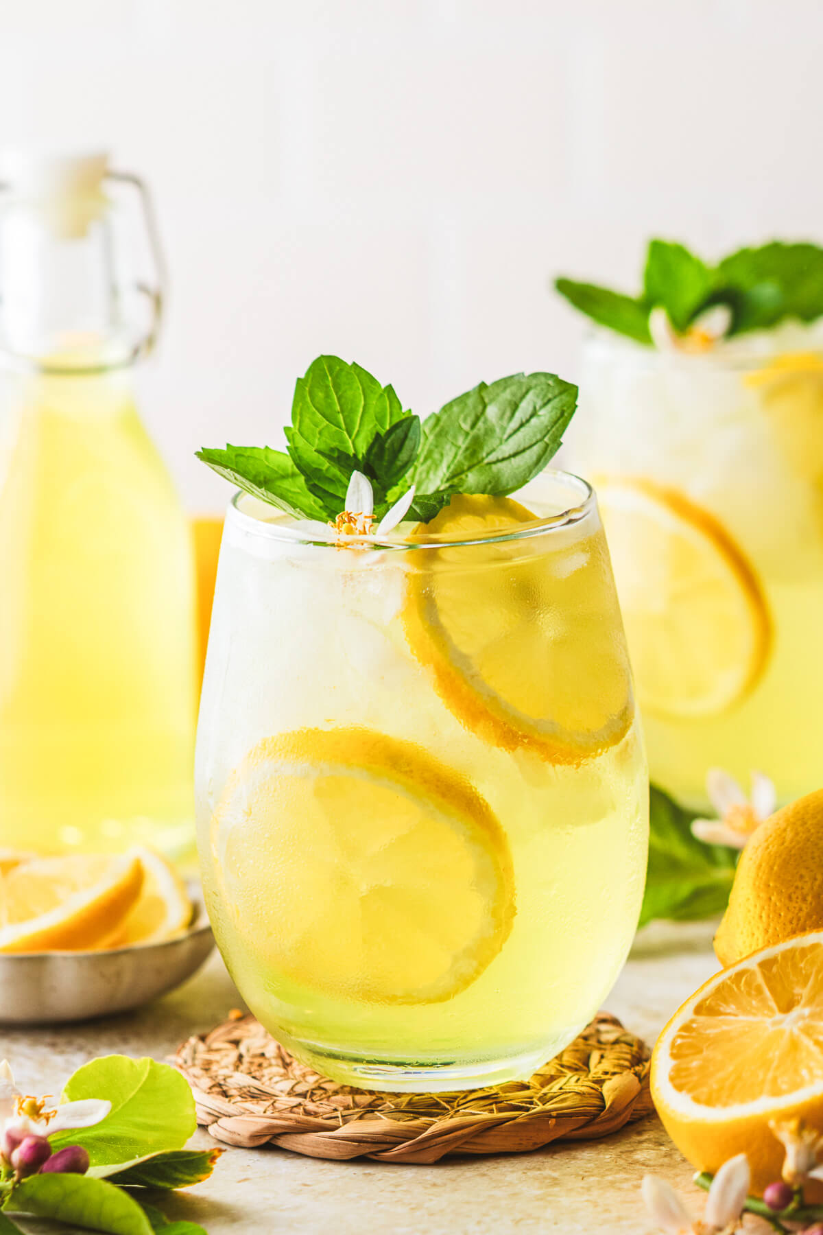 Two sunny yellow cockails in stemless wine glasses garnished with fresh mint and lemon slices.