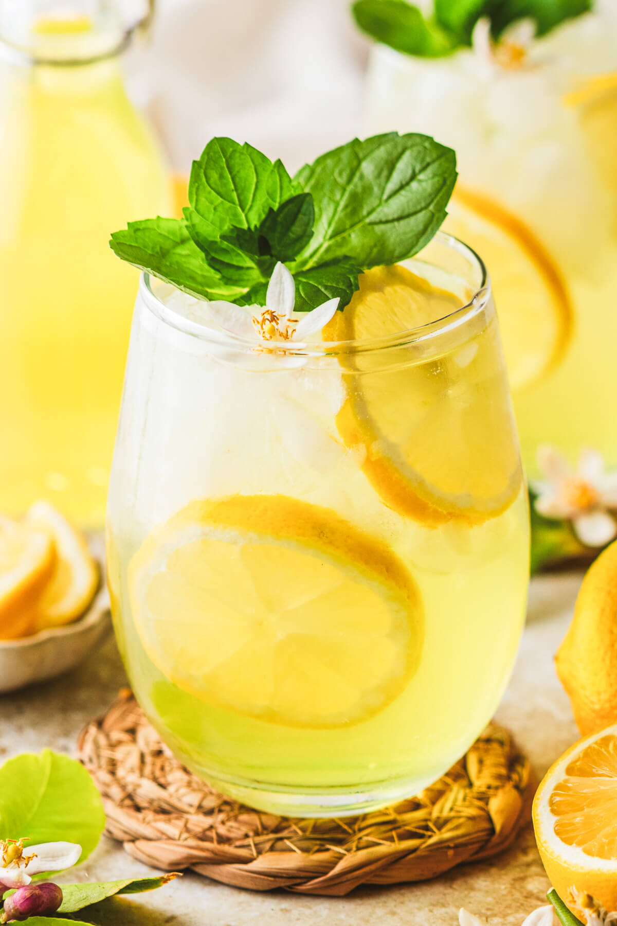 A sunny yellow cockail in a stemless wine glass garnished with fresh mint and lemon slices.