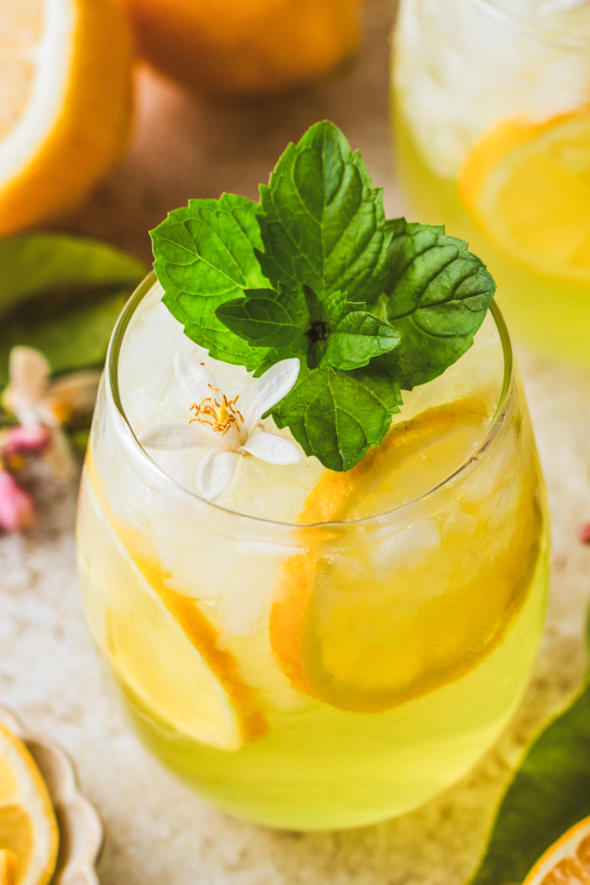 A sunny yellow cockail in a stemless wine glass garnished with fresh mint and lemon slices.