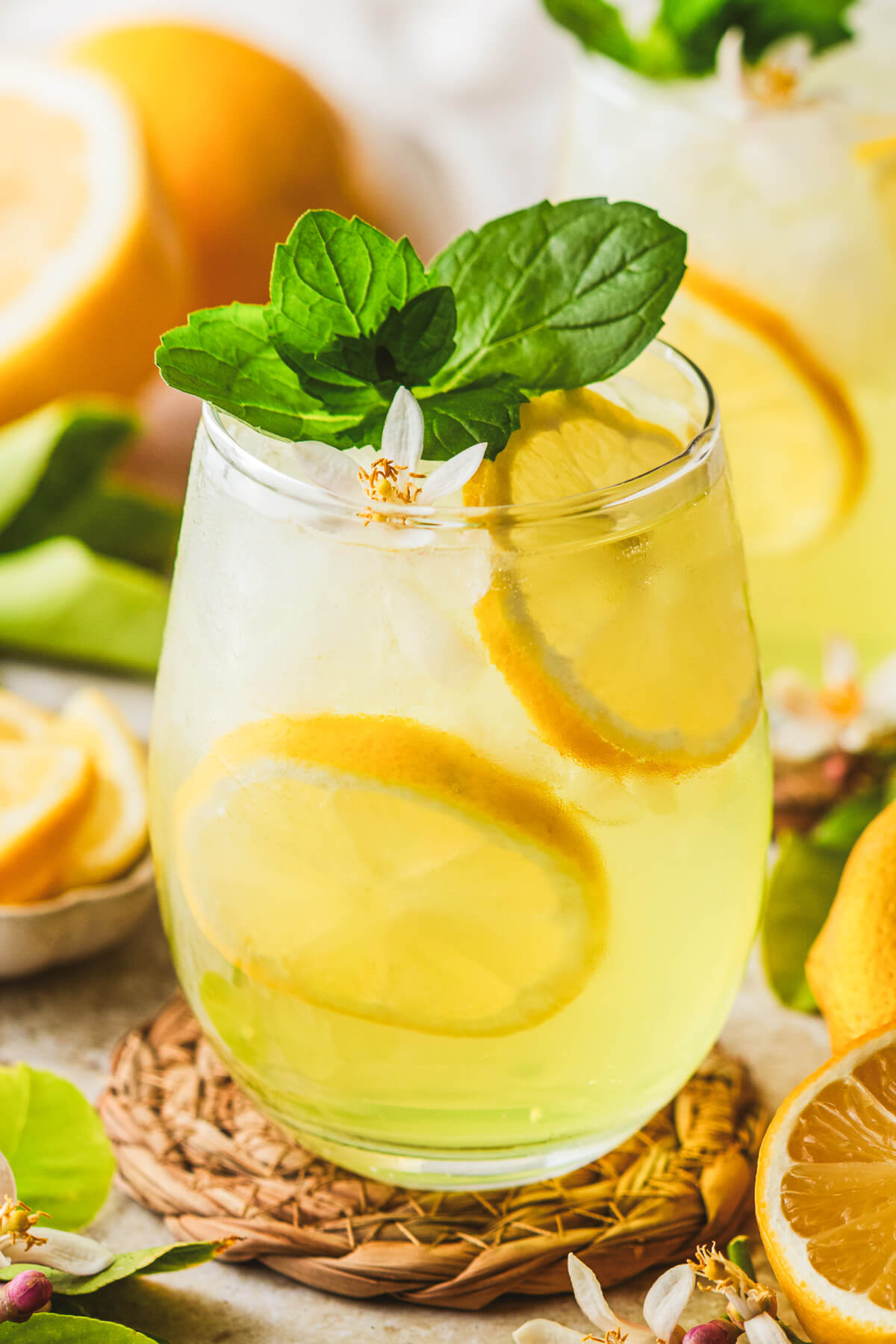 A stemless wine glass filled with a sunny yellow Limoncello Spritz garnished with lemon slices and a sprig of mint.