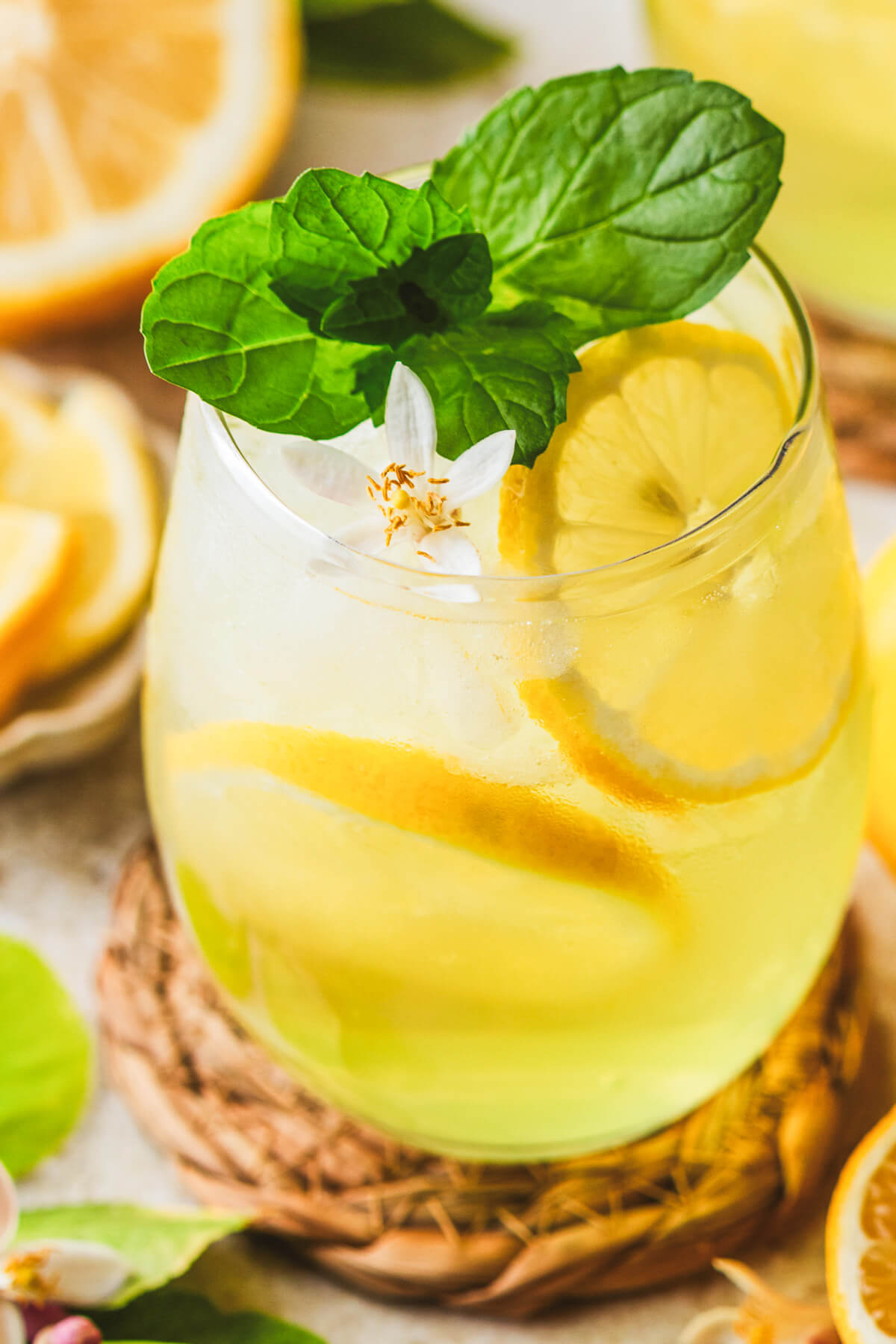 A sunny yellow cockail in a stemless wine glass garnished with fresh mint and lemon slices.