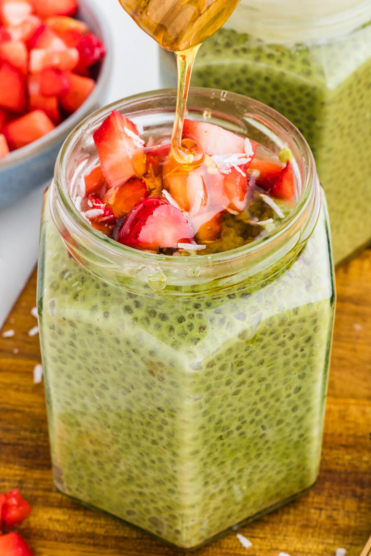 Honey is drizzled over the sliced strawberries topping a jar of vibrant green Match Chia Pudding.