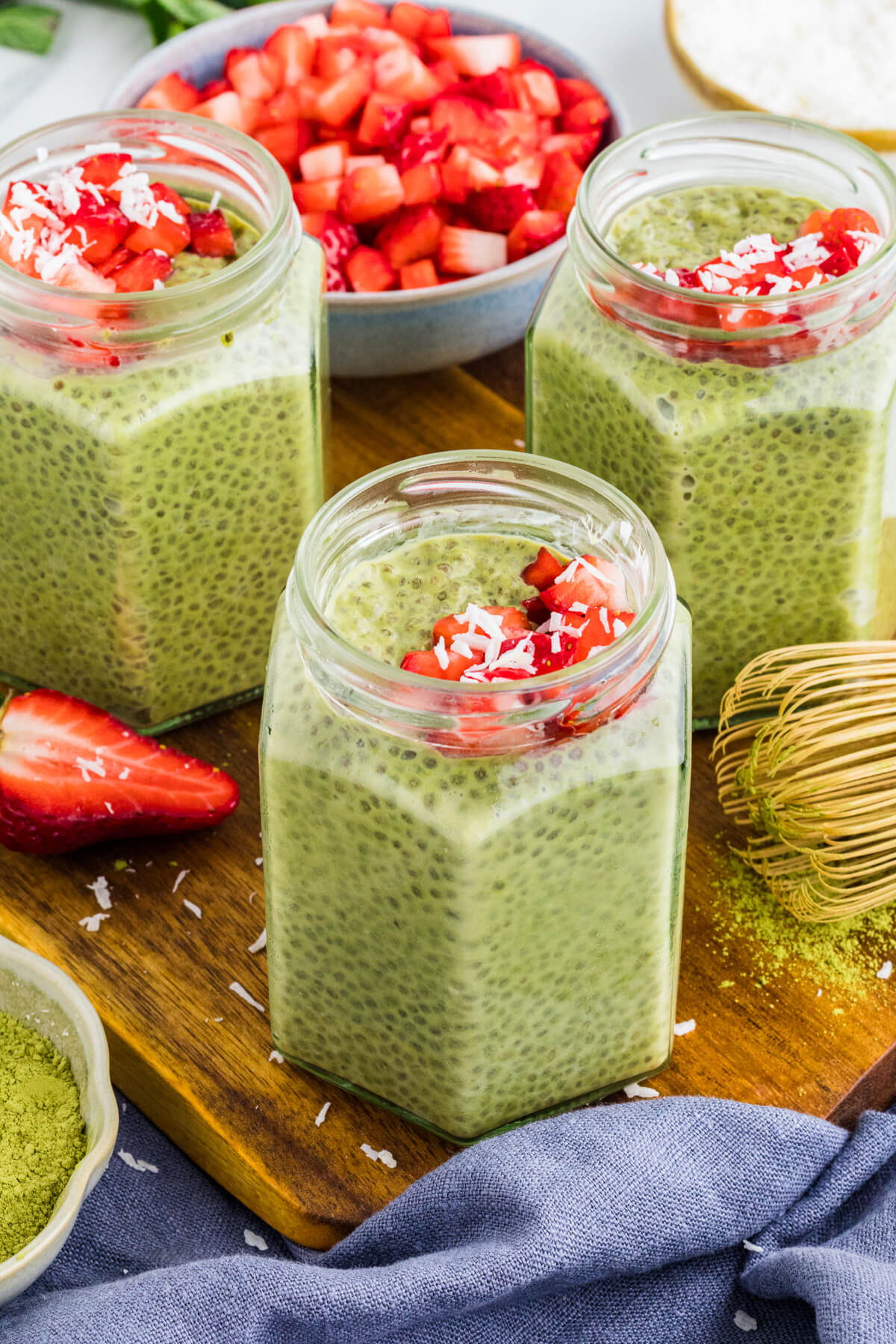 Three jars of vibrant green Match Chia Pudding topped with sliced strawberries and coconut flakes.