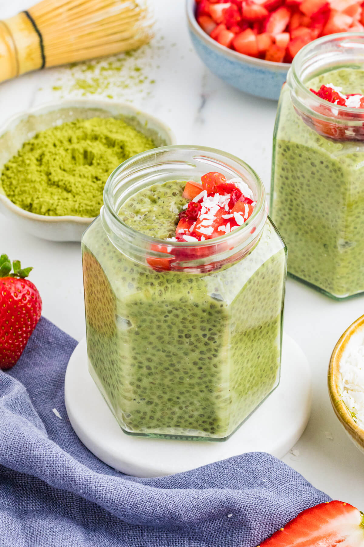 Two jars of vibrant green Match Chia Pudding topped with sliced strawberries and coconut flakes.