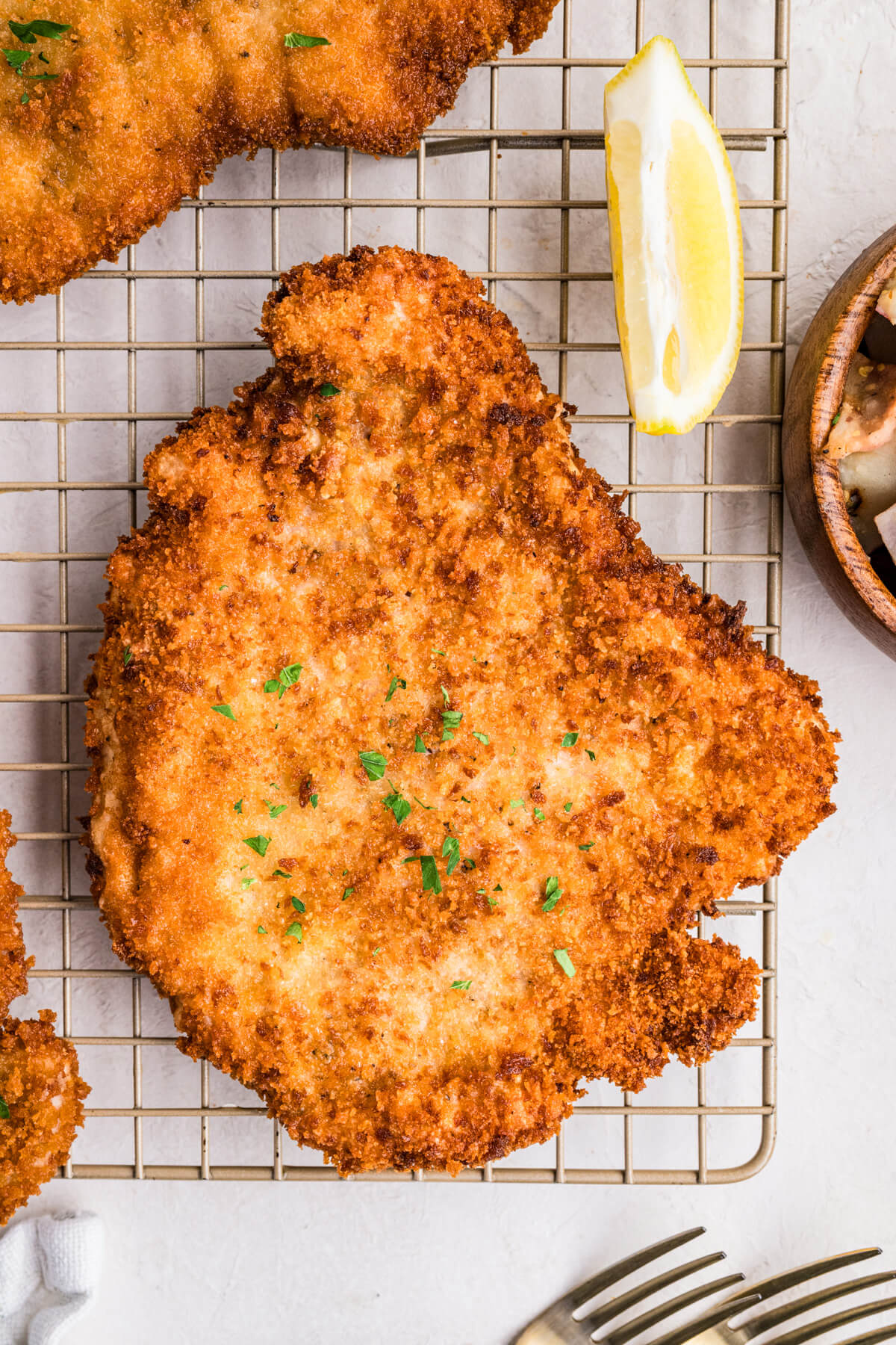 Two golden fried pork schnitzels with lemon wedges on a wire rack.