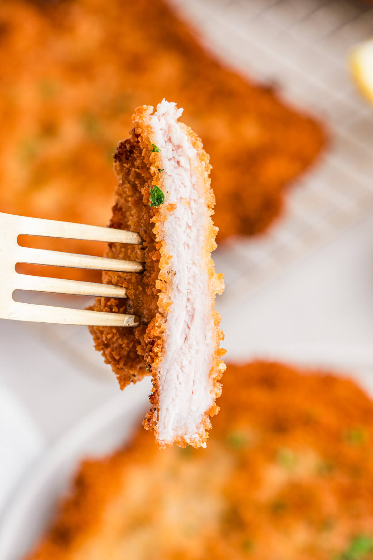 A fork holds a bite of pork schnitzel showing the juicy interior.